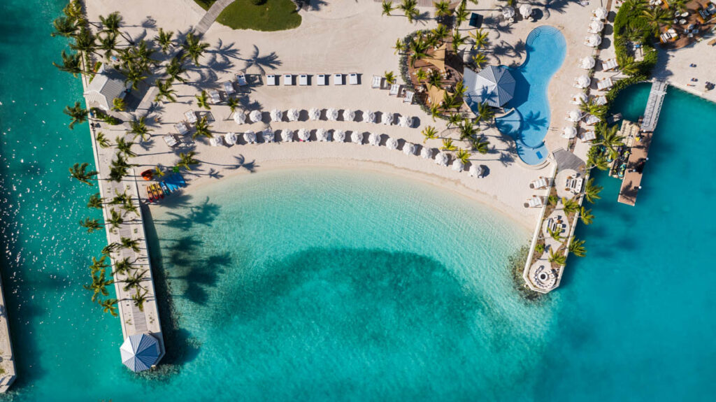 Drone aerial view of Blue Haven's private beach with clear turquoise water, sea kayaks, beach chairs and beachfront pool with swim-up bar.