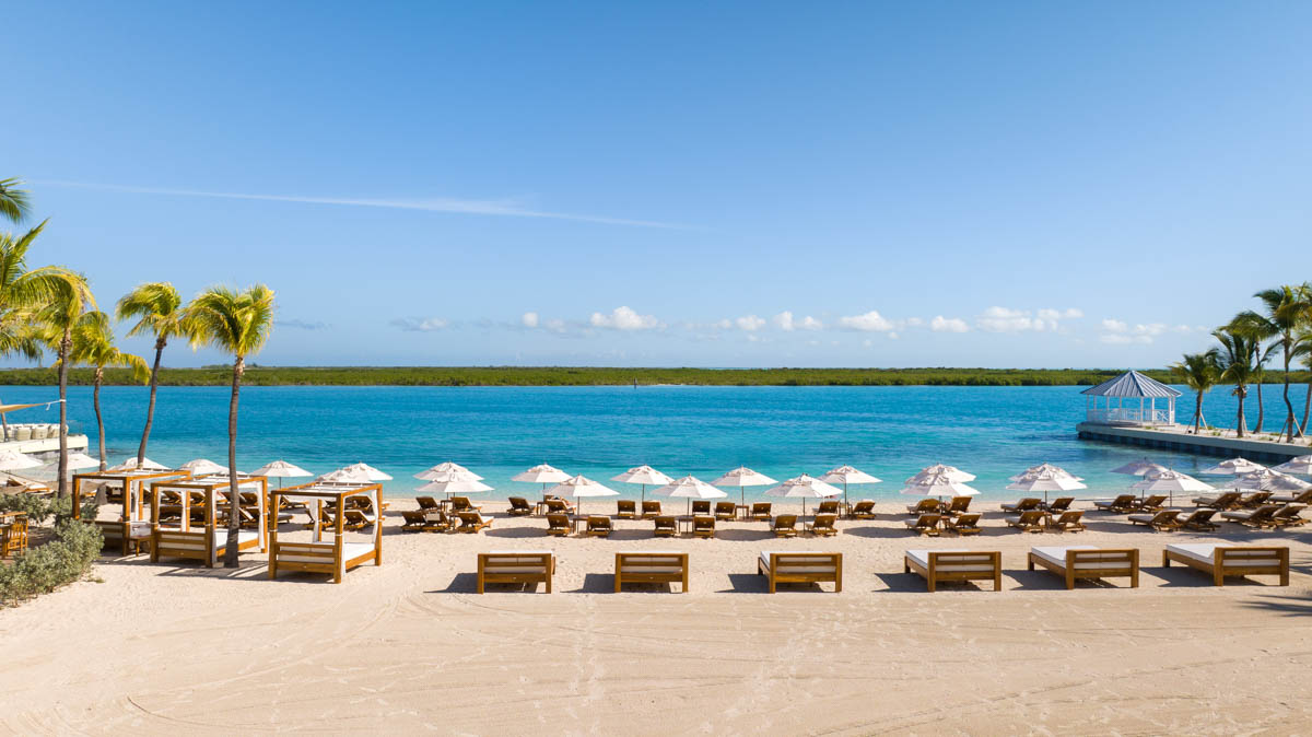 Ocean-facing view from Blue Haven's private beach with outdoor daybeds, beach lounge chairs and sun umbrellas and view of Mangrove Cay in the distance.